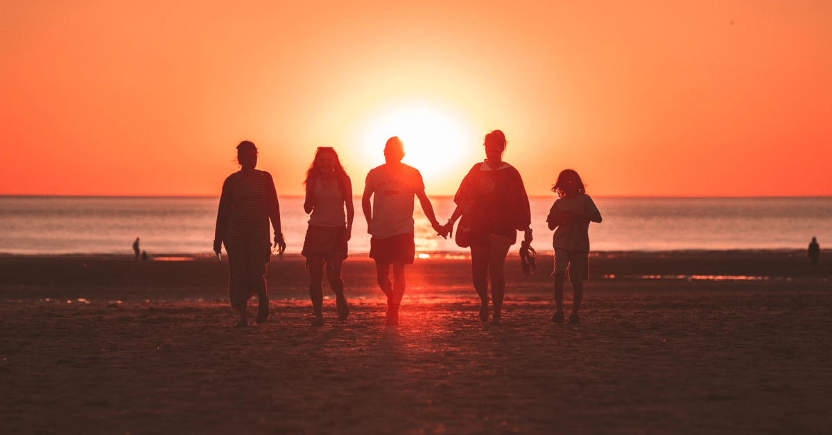 Four adults and a child walking on the beach during a sunset - Expanding Wallet
